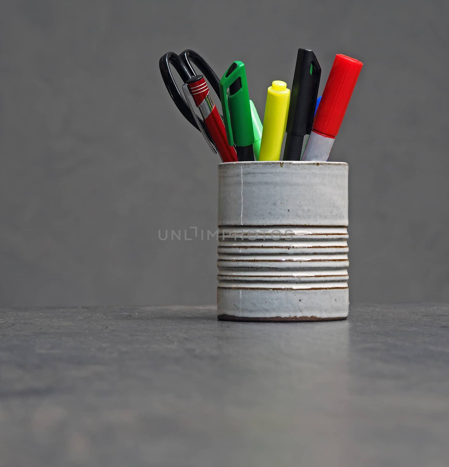 color office equipment in grey ceramic cup - markers, pen and scissors on grey background