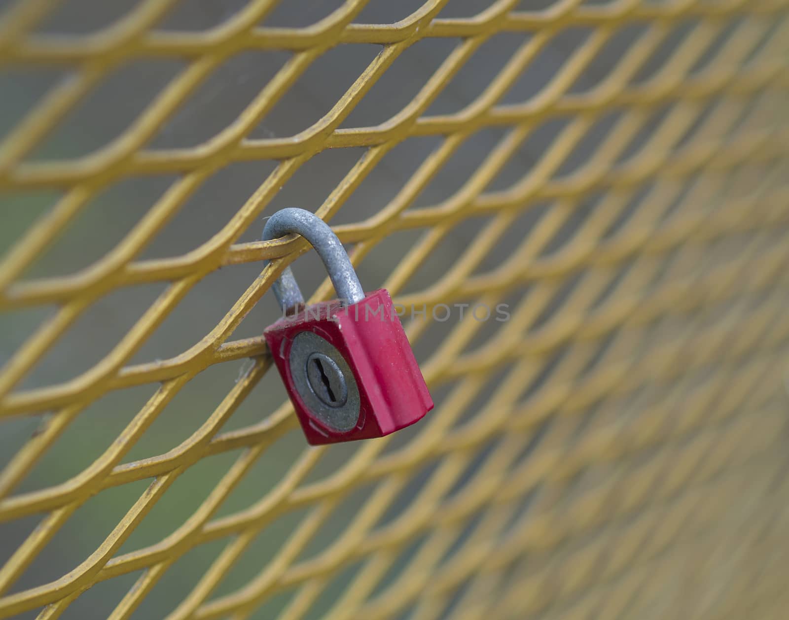 close up old red lock hanging locked on the yellow metal grating