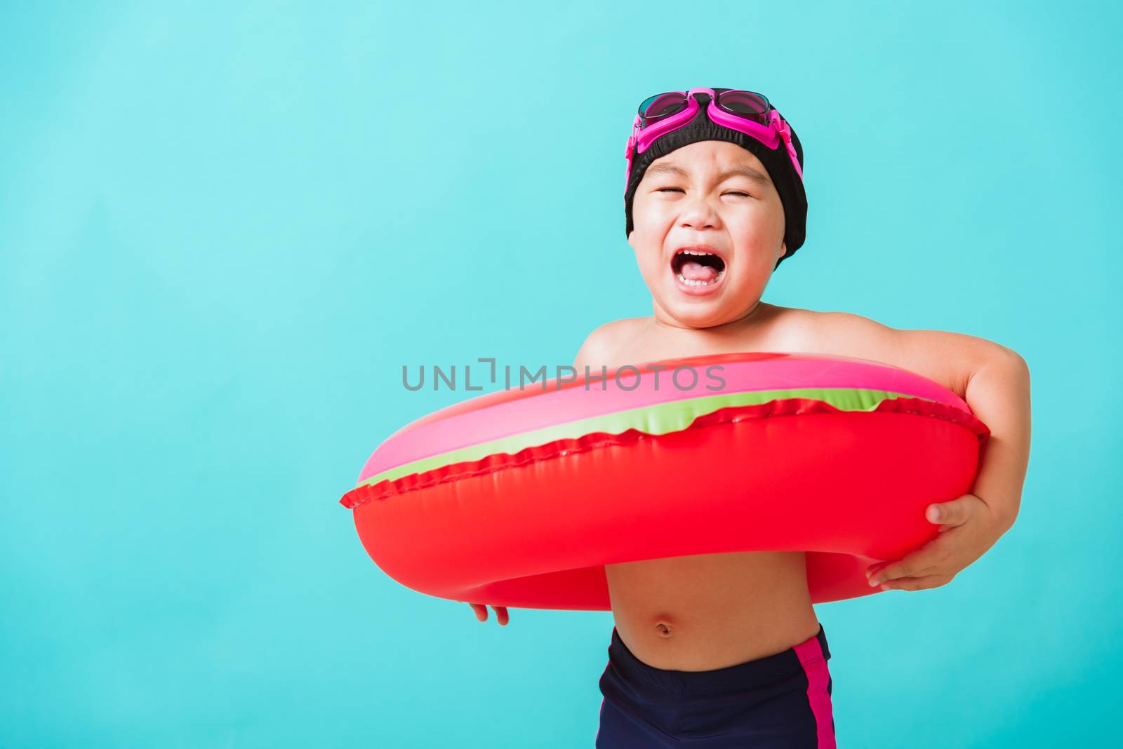 Summer vacation concept, Portrait Asian happy cute little child boy wear goggles and swimsuit hold watermelon inflatable ring, Kid having fun on summer vacation, studio shot isolated blue background