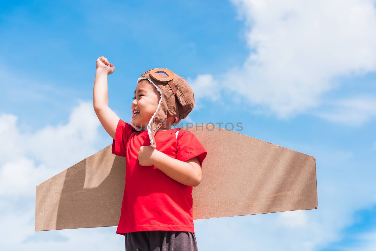 Happy Asian funny child or kid little boy smile wear pilot hat and goggles play toy cardboard airplane wing flying raises hand up against summer blue sky cloud background, Startup freedom concept
