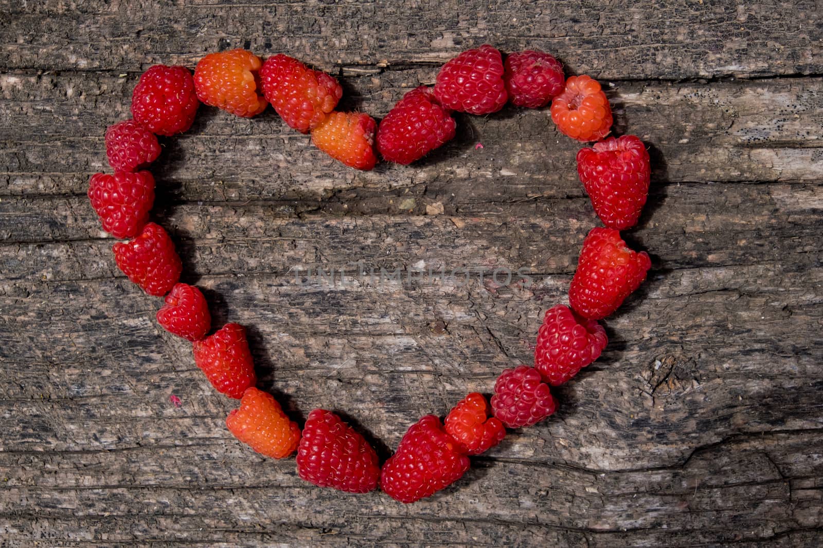 Heart made of ripe aromatic raspberrie on a wooden background.