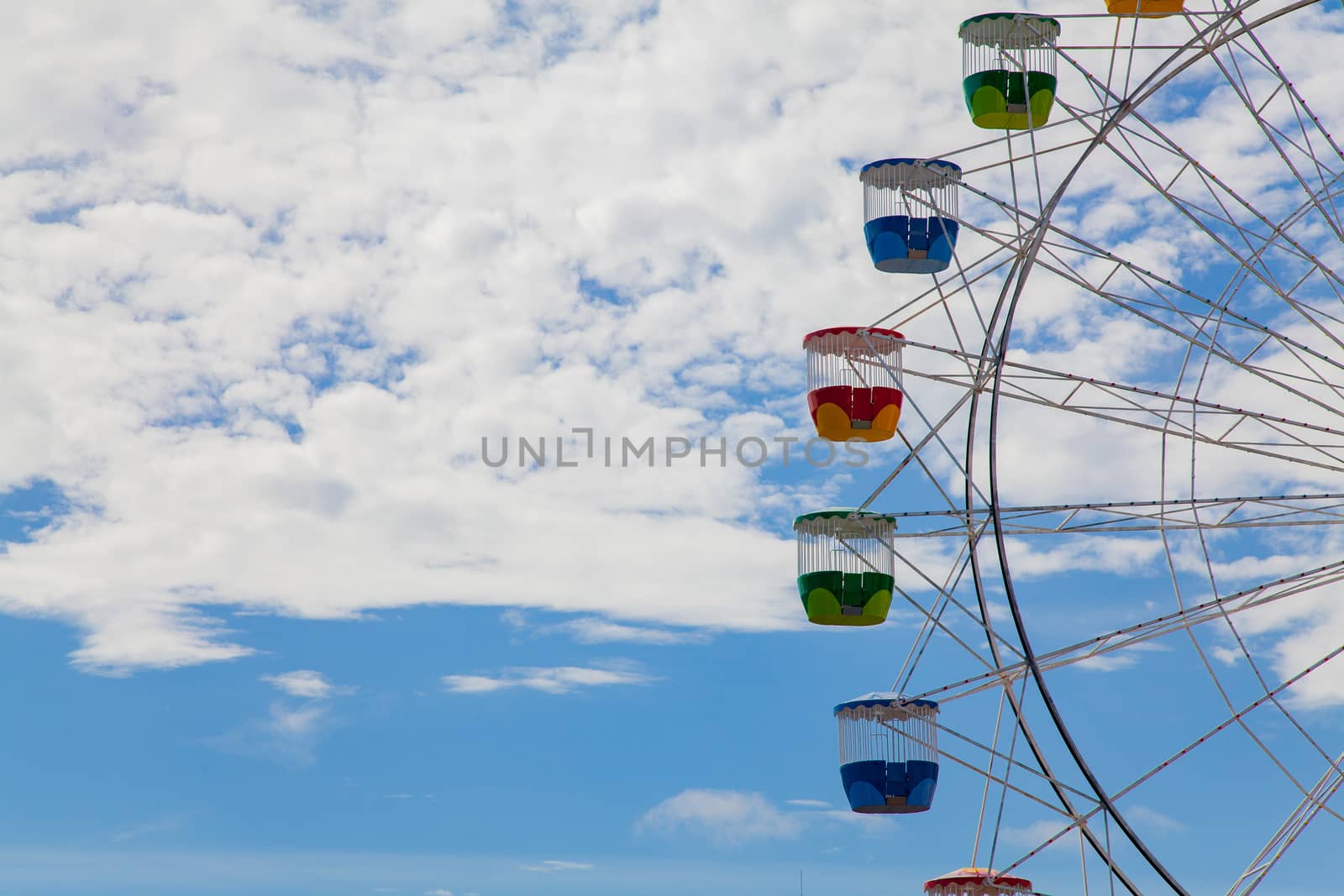 Gondolas of ferris wheel, very colourful, against blue sky with clouds by kgboxford