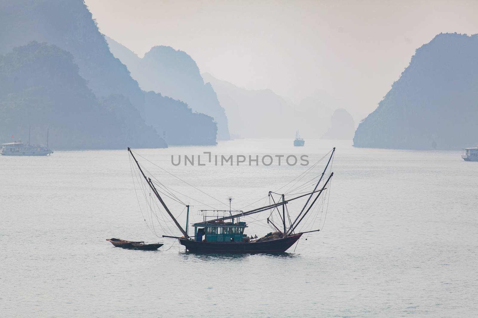 Ha Long Bay, Vietnam, is a World Heritage Site and very popular with tourists. Thousands of towering limestone islands topped by rainforests rising up out of the emerald seas. Cruise ships take tourists for day trips and overnight stays in the bay. Traditional fishing boats against blue mountains, . High quality photo