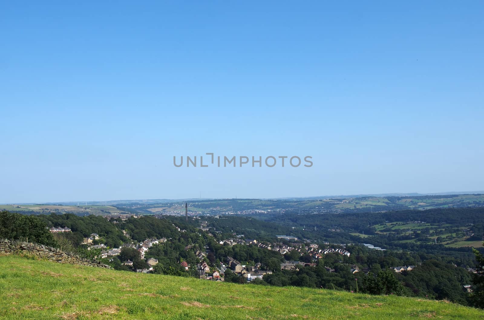 a panoramic view of halifax from above surrounded by Fields and pennine hills and a blue summer sky