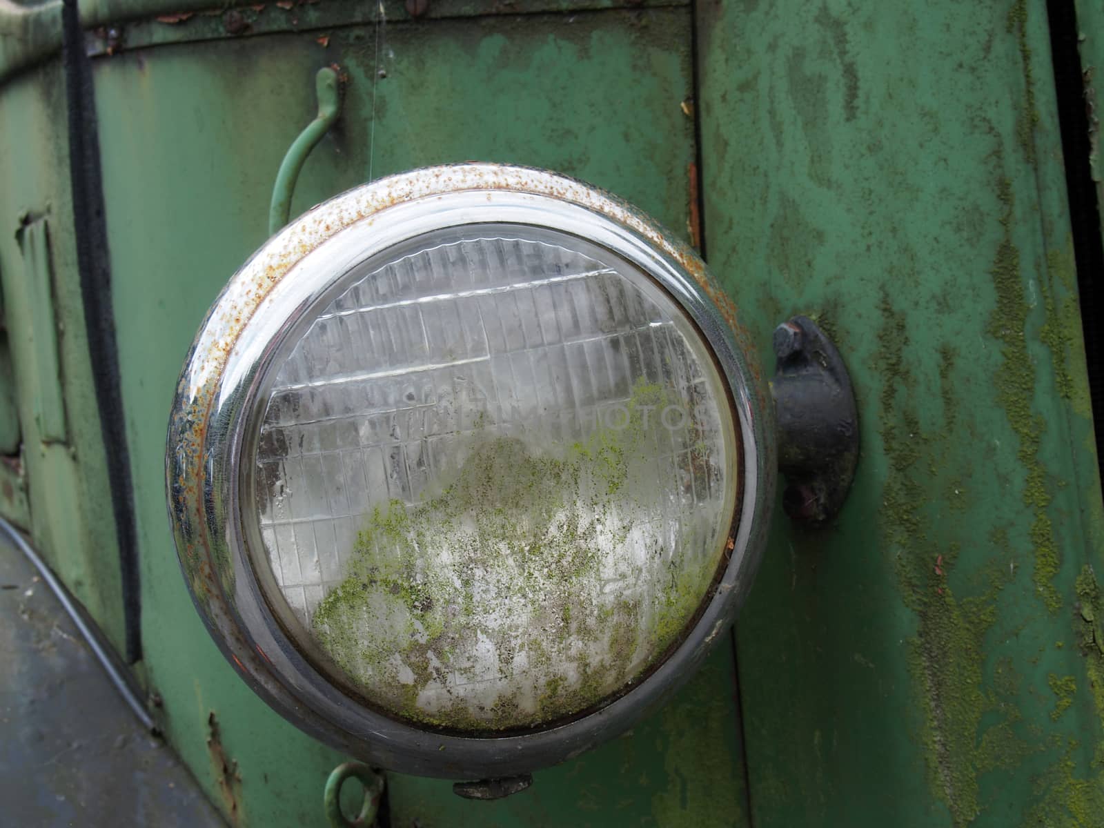close up of the headlight of an old abandoned truck with rusted green grille and panels