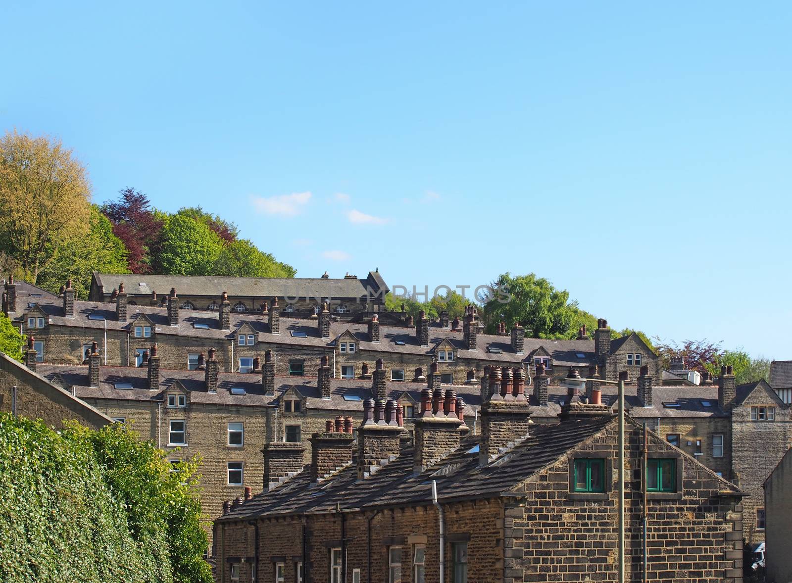 streets of terraced stone houses on a hillside surrounded by trees with a blue summer sky in hebden bridge west yorkshire
