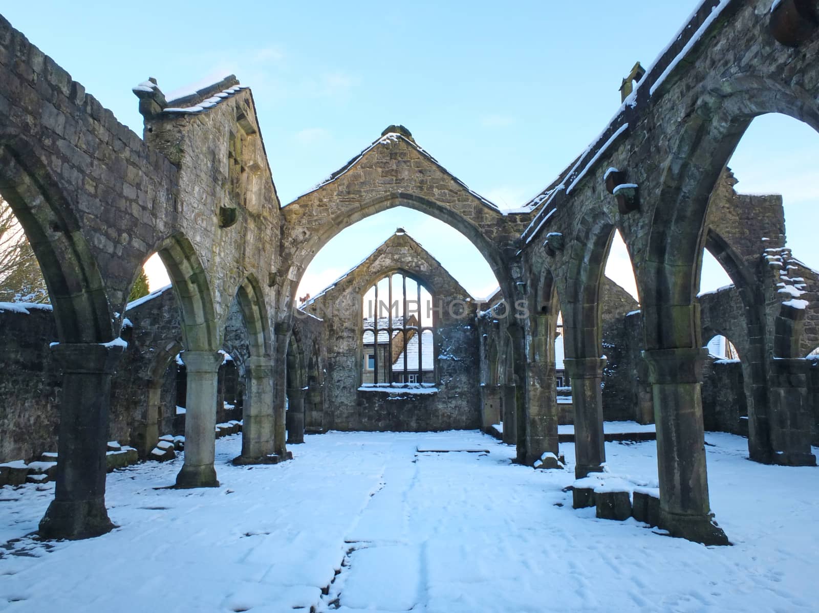 the medieval ruined church in heptonstall covered in snow showing arches and columns against a blue winter sky