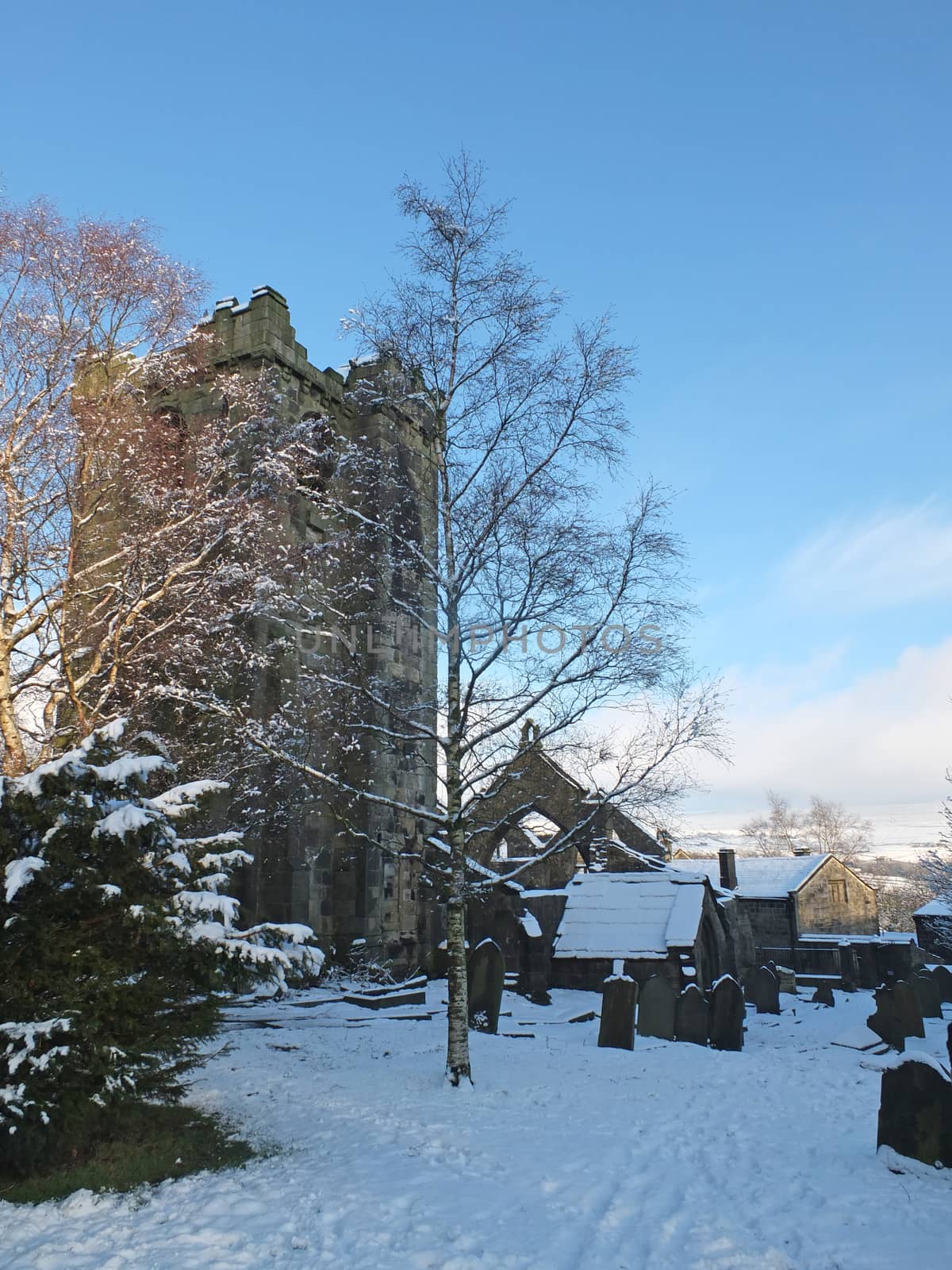 a scenic view of the medieval ruined church in the village of heptonstall west yorkshire covered in snow with surrounding graves trees and houses