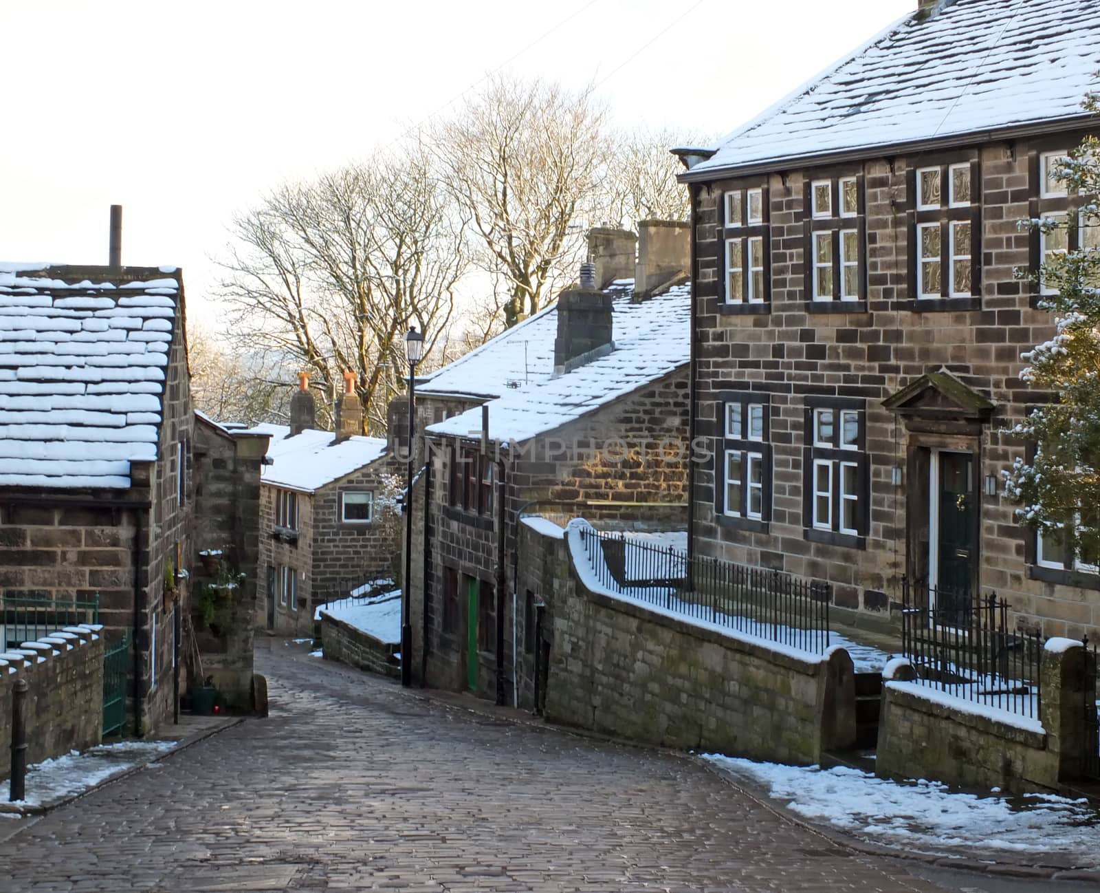 A scenic view of the main street in the village of heptonstall in west yorkshire with snow covering the old stone houses and pennine scenery visible in the background