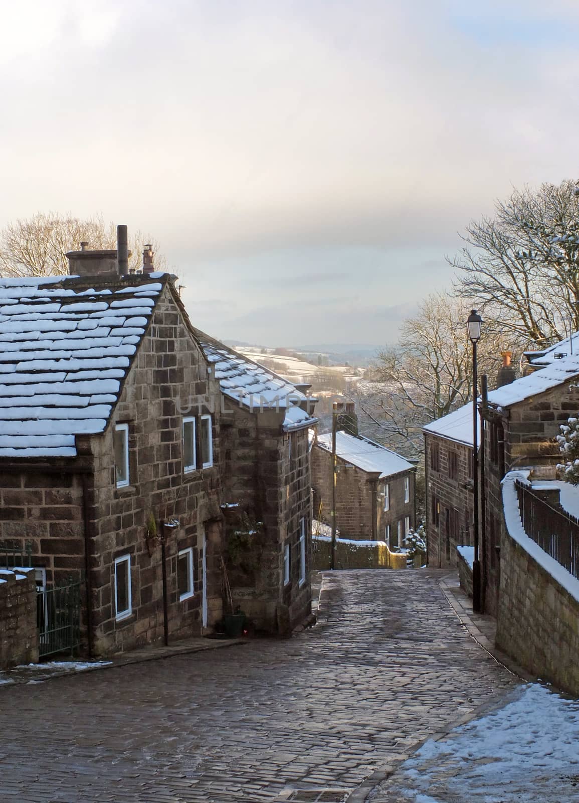 A scenic view of the main street in the village of heptonstall in west yorkshire with snow covering the old stone houses and pennine scenery visible in the background by philopenshaw