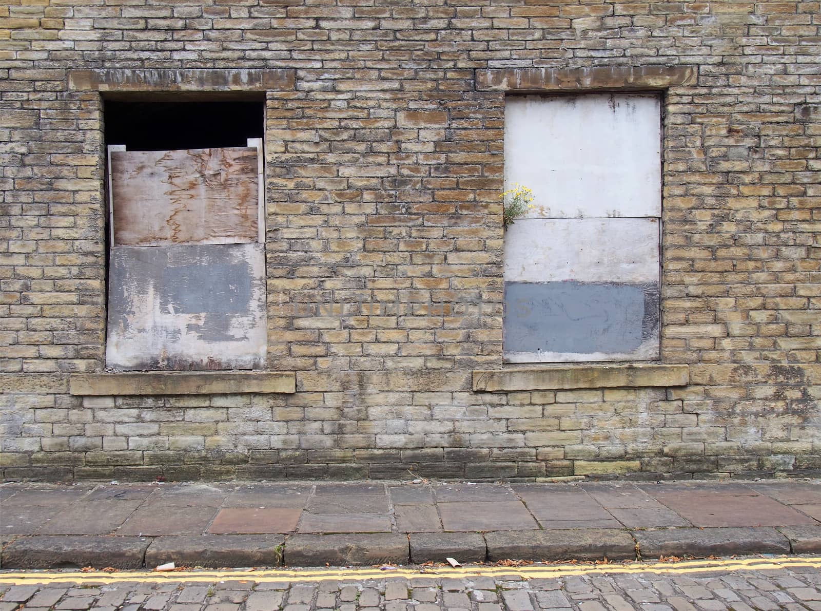 front view of an old abandoned derelict house on an empty street with boarded up windows and dilapidated brick walls by philopenshaw