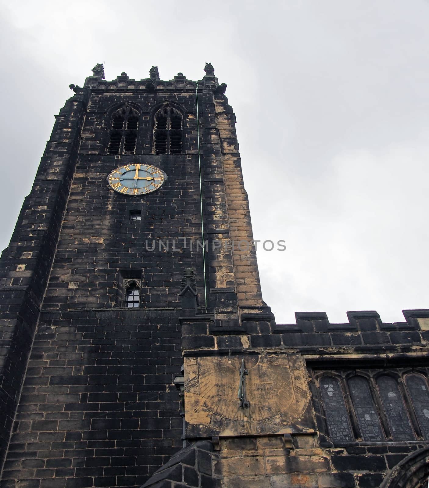 a view of halifax minster in west yorkshire with dark stonework on the medieval church tower and clock