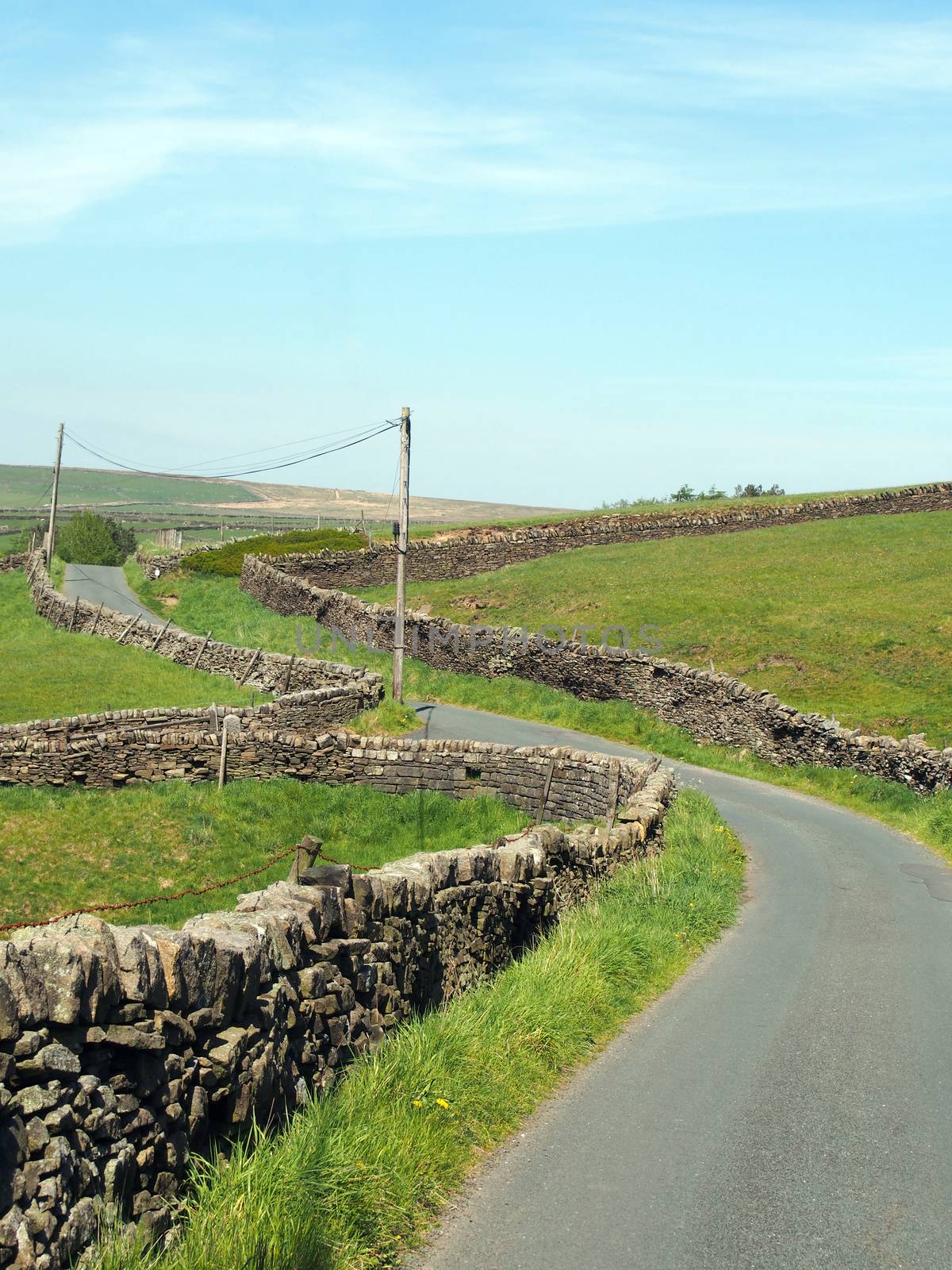 a junction on a winding narrow country lane bordered by dry stone walls in hilly yorkshire dales countryside with blue summer sky on the old howarth road by philopenshaw