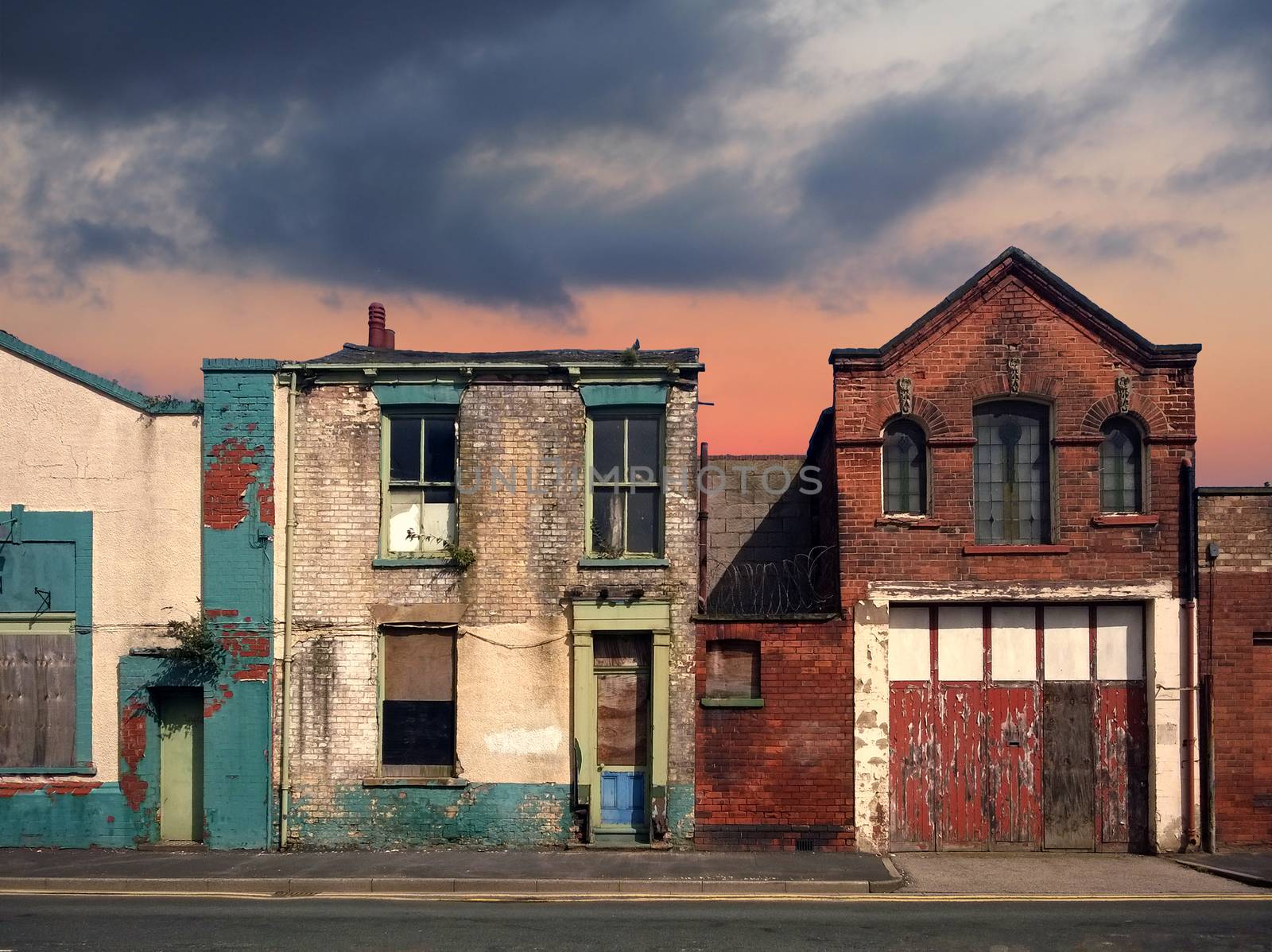 a deserted street of old abandoned ruined houses with bright peeling paint and crumbling brickwork in evening sunlight against a bright cloudy sunset sky redevelopment or fantasy concept