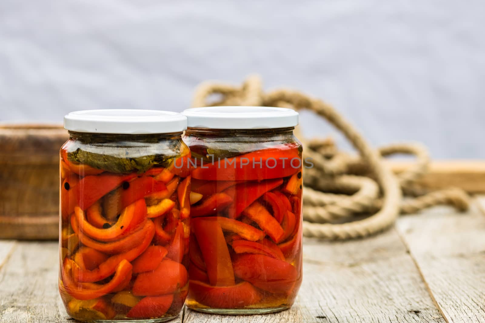 Glass jars with pickled red bell peppers.Preserved food concept, canned vegetables isolated in a rustic composition.