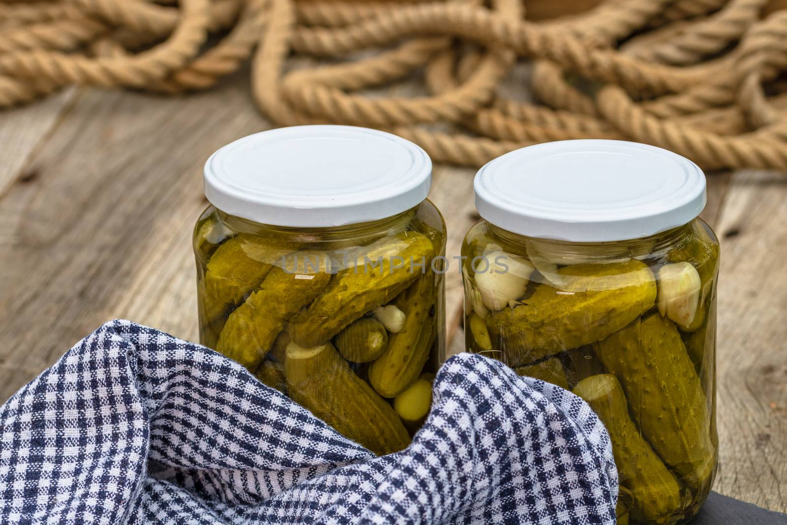 Glass jars with pickled red bell peppers and pickled cucumbers (pickles) isolated. Jars with variety of pickled vegetables. Preserved food concept in a rustic composition.