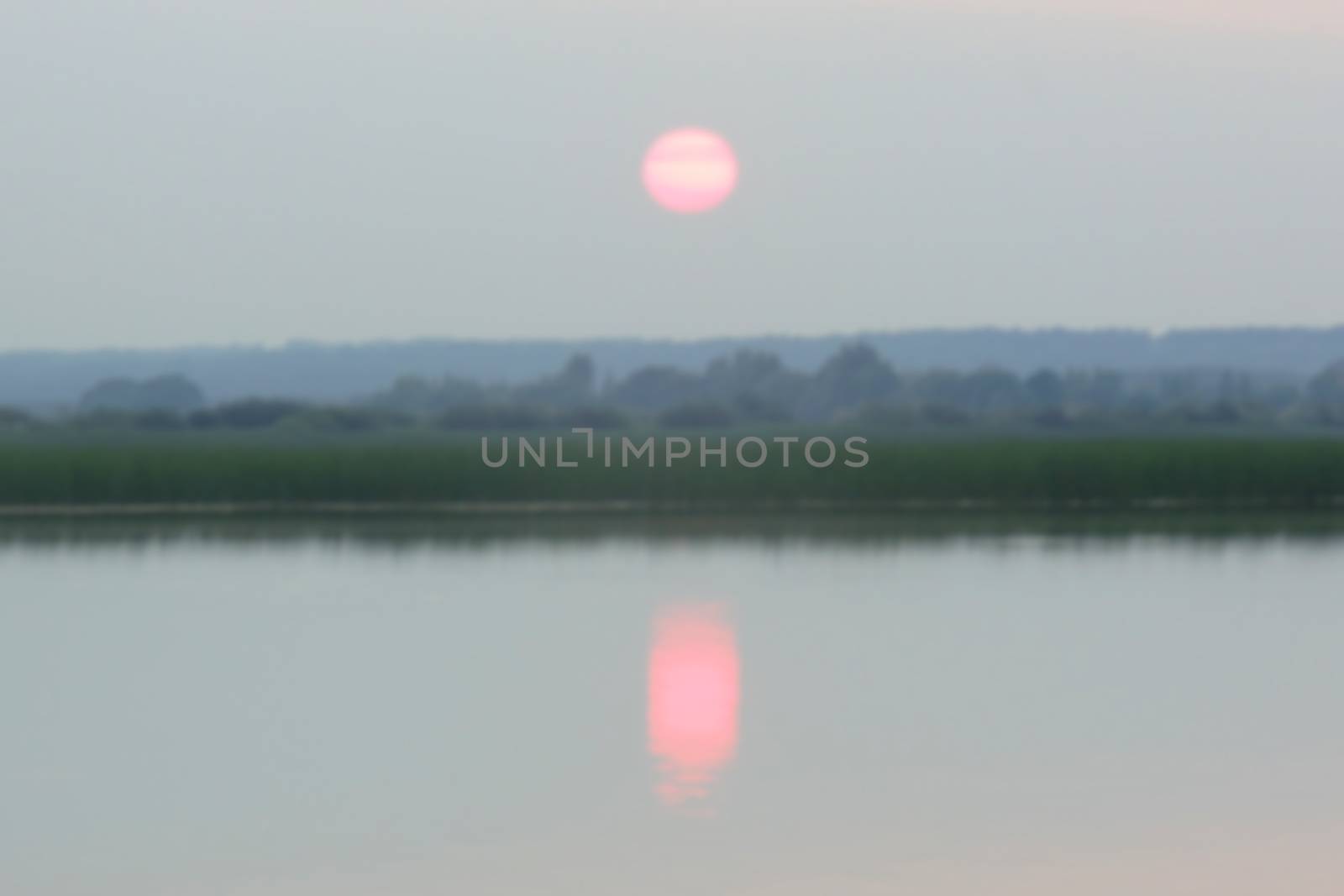 pink sunset in the haze over the lake and forest, blurred photo