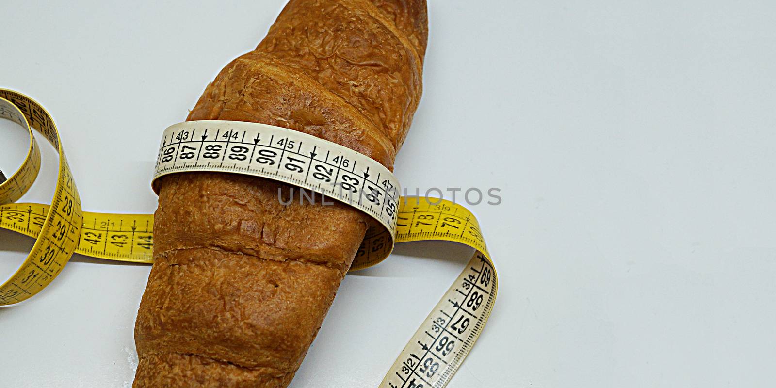 soft measuring ruler wrapped around a croissant as a symbol of unhealthy nutrition, copy space