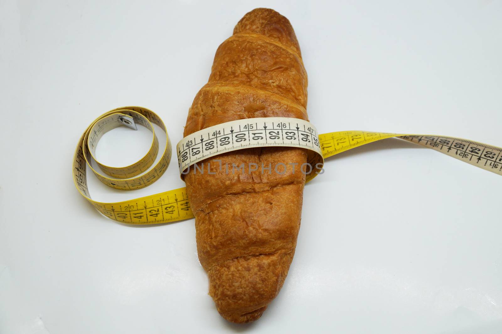 soft measuring ruler wrapped around a croissant as a symbol of unhealthy nutrition, on a white background