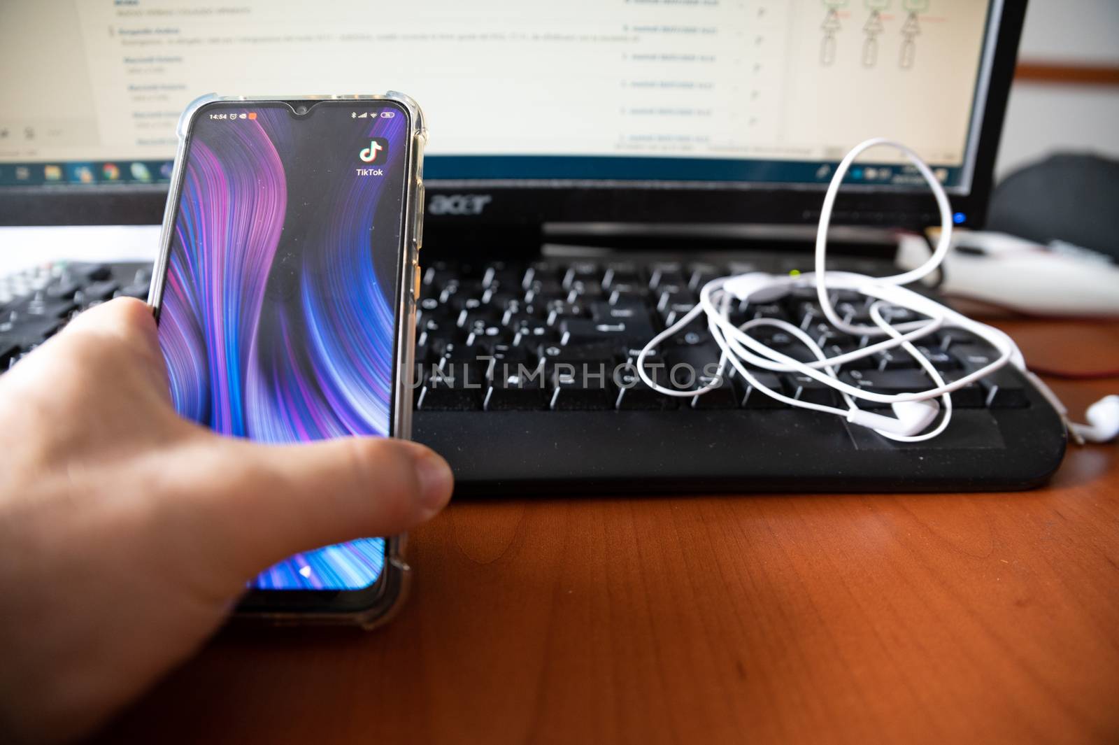 Turin, Piedmont, Italy. July 2020. Against the background of a workplace, close-up image of the smartphone display: the logo of the Tik Tok application is highlighted, the finger is about to touch it.