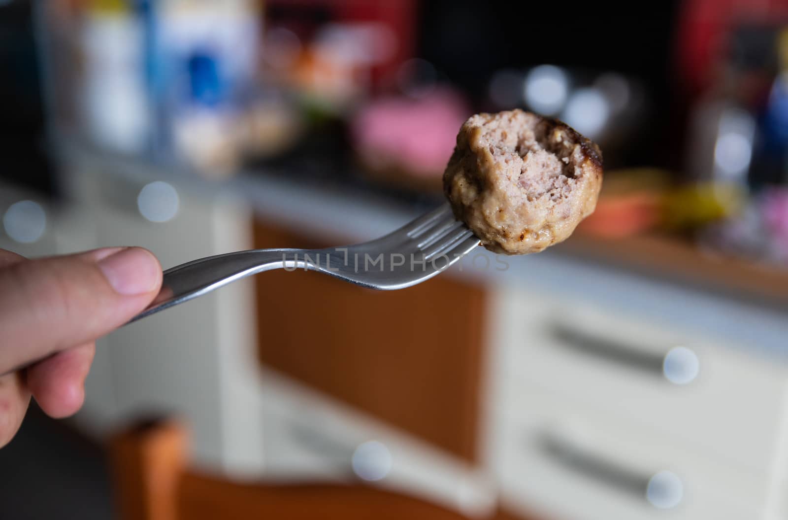 In the blurred background of a kitchen a close-up image of a meatball skewered by a fork. A bite was eaten.