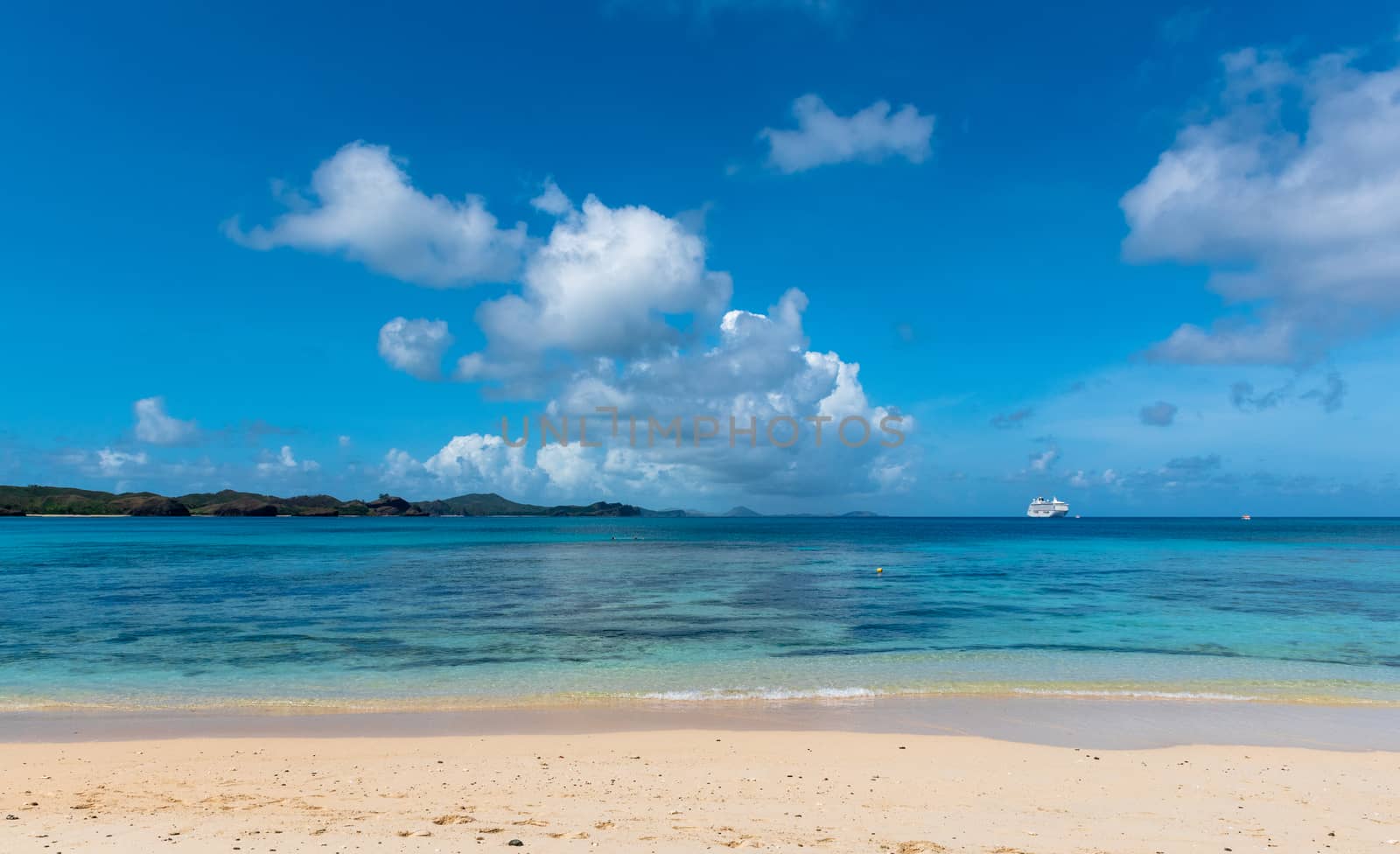 Wide angle landscape photo with a cruise ship anchored off Fiji on a beautiful summer day.