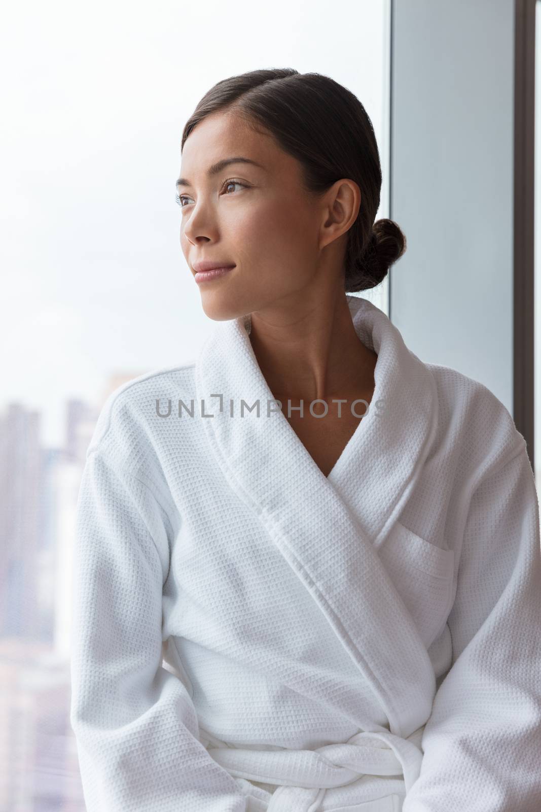 Asian woman relaxing at luxury hotel spa wearing bathrobe looking at window portrait. Pampering travel lifestyle at resort.