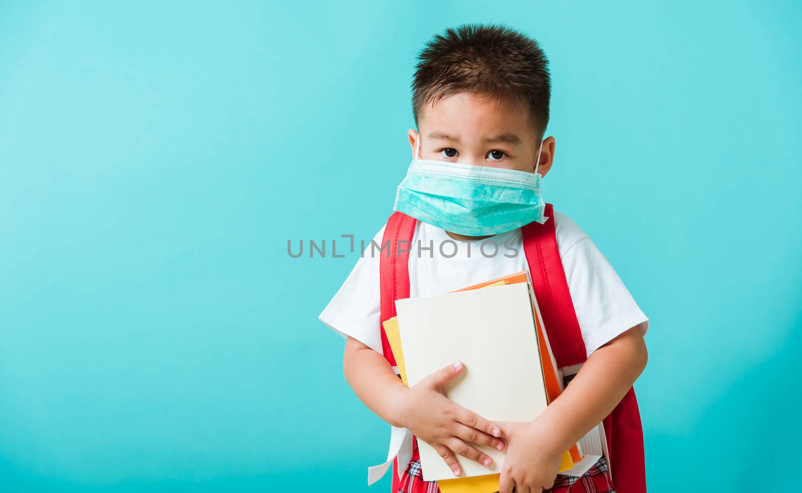 Back to school coronavirus Covid-19 education. Portrait Asian little child boy kindergarten wear face mask protective and school bag hold book before going to school, studio shot isolated background