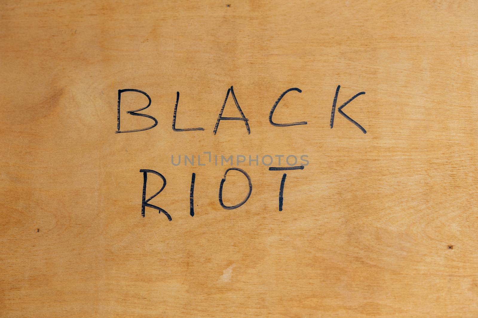 The words black riot handwritten with black paint marker on flat plywood surface. Concept of street disorders in 2020.