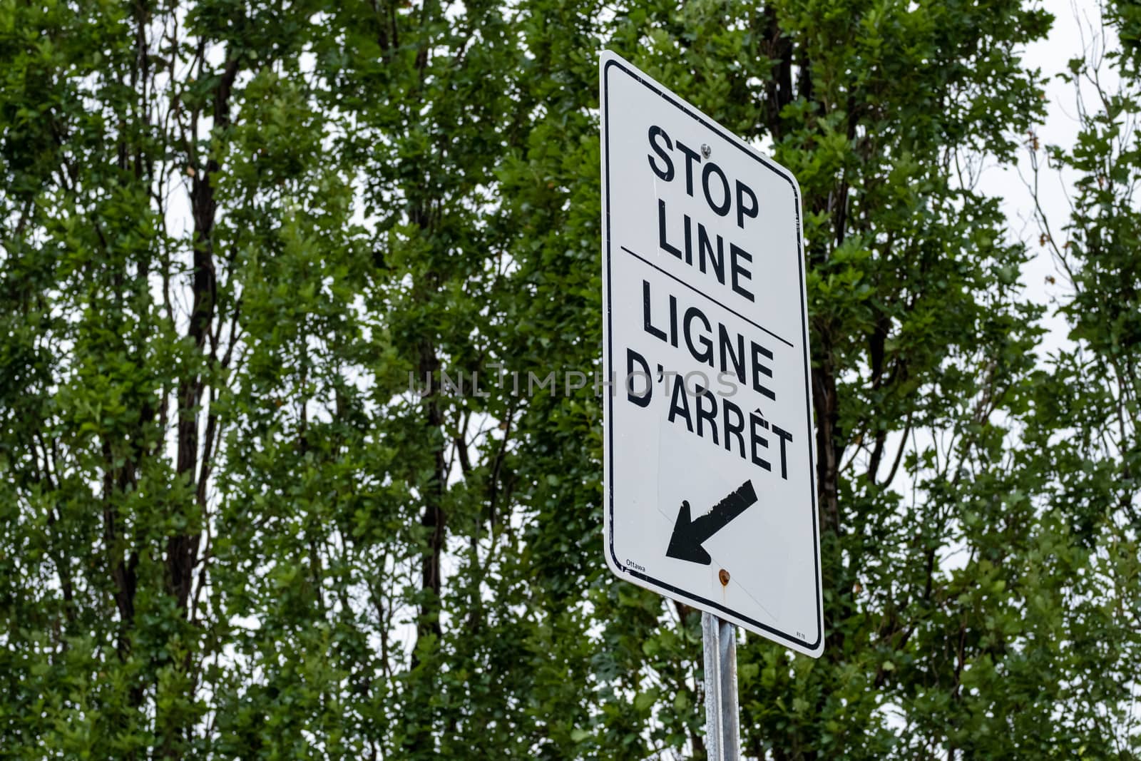 A bilingual sign indicates the location of a stop line for a traffic intersection with an arrow and labels in English and French languages.
