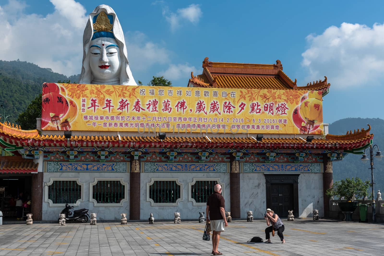 Penang, Malaysia -- March 7, 2016.  A tourist poses for a photo by a large statue of the Buddha.