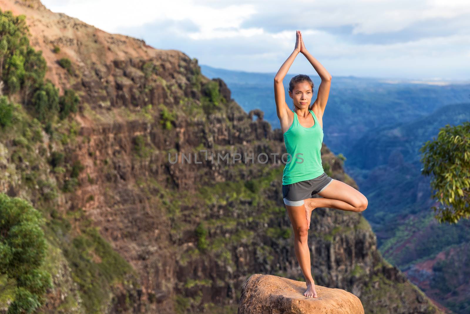 Woman doing yoga in Hawaii mountains. Asian girl meditating in tree pose with praying hands above head standing on one leg in Kauai, Hawaii, USA. girl in serene nature landscape.