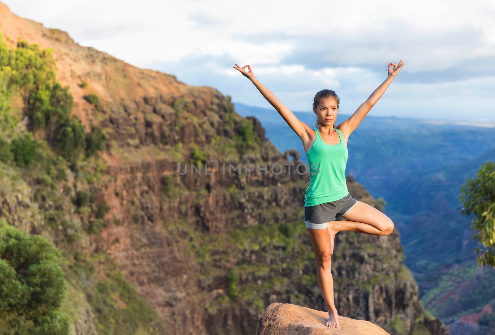 Yoga meditation - woman meditating doing yoga tree balance pose with open branch arms balancing on rock in Kauai mountains, Hawaii, USA. Serene relaxing girl in nature landscape in Waimea Canyon.