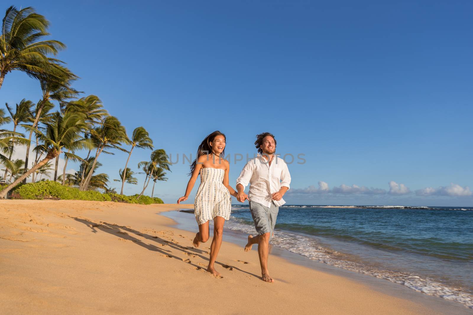 Happy couple relaxing running together on beach. Young multiracial people having fun during sunset on tropical vacation. Summer travel destination.