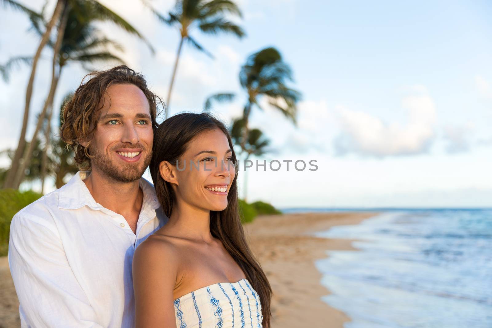 Couple enjoying Hawaii vacations on hawaiian beach. Portrait of beautiful Asian chinese woman and Caucasian man happy smiling relaxing in Kauai, USA.