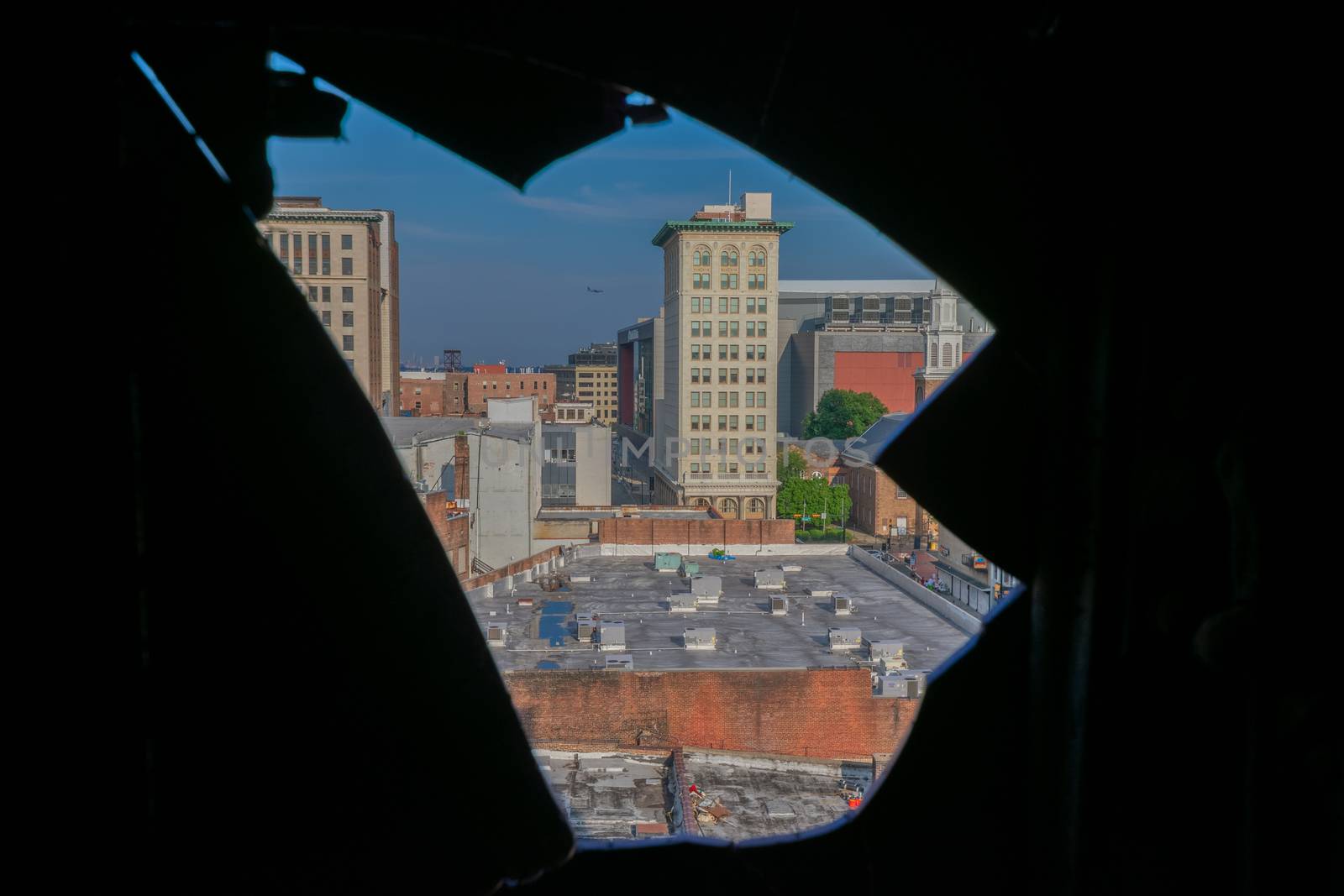 Looking Out a Hole in a Window at a City Skyline With an Airplane Flying Through