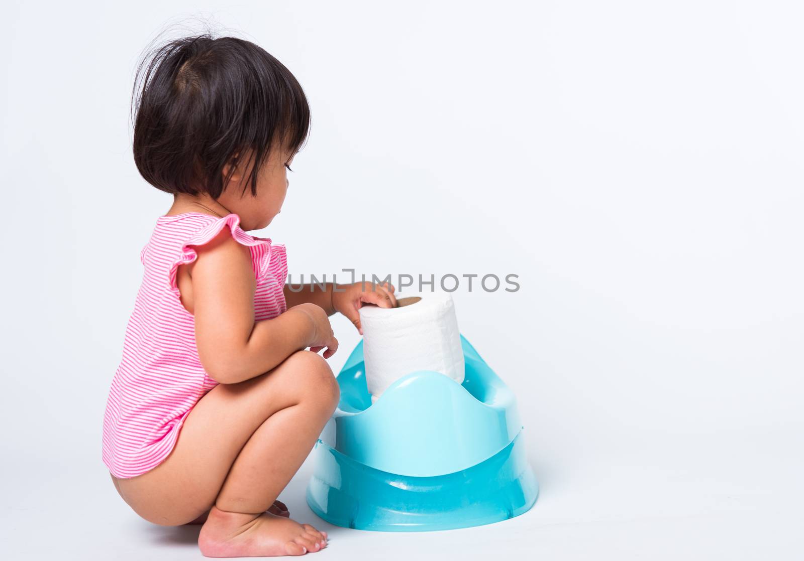 Asian little cute baby child girl education training to sitting on blue chamber pot or potty with toilet paper rolls, studio shot isolated on white background, wc toilet concept