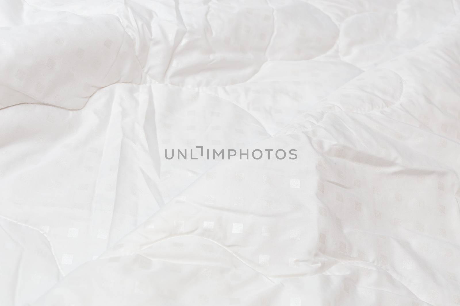 White fabric blanket with one big fold close-up backdrop with selective focus and background blur. Small white squares pattern.