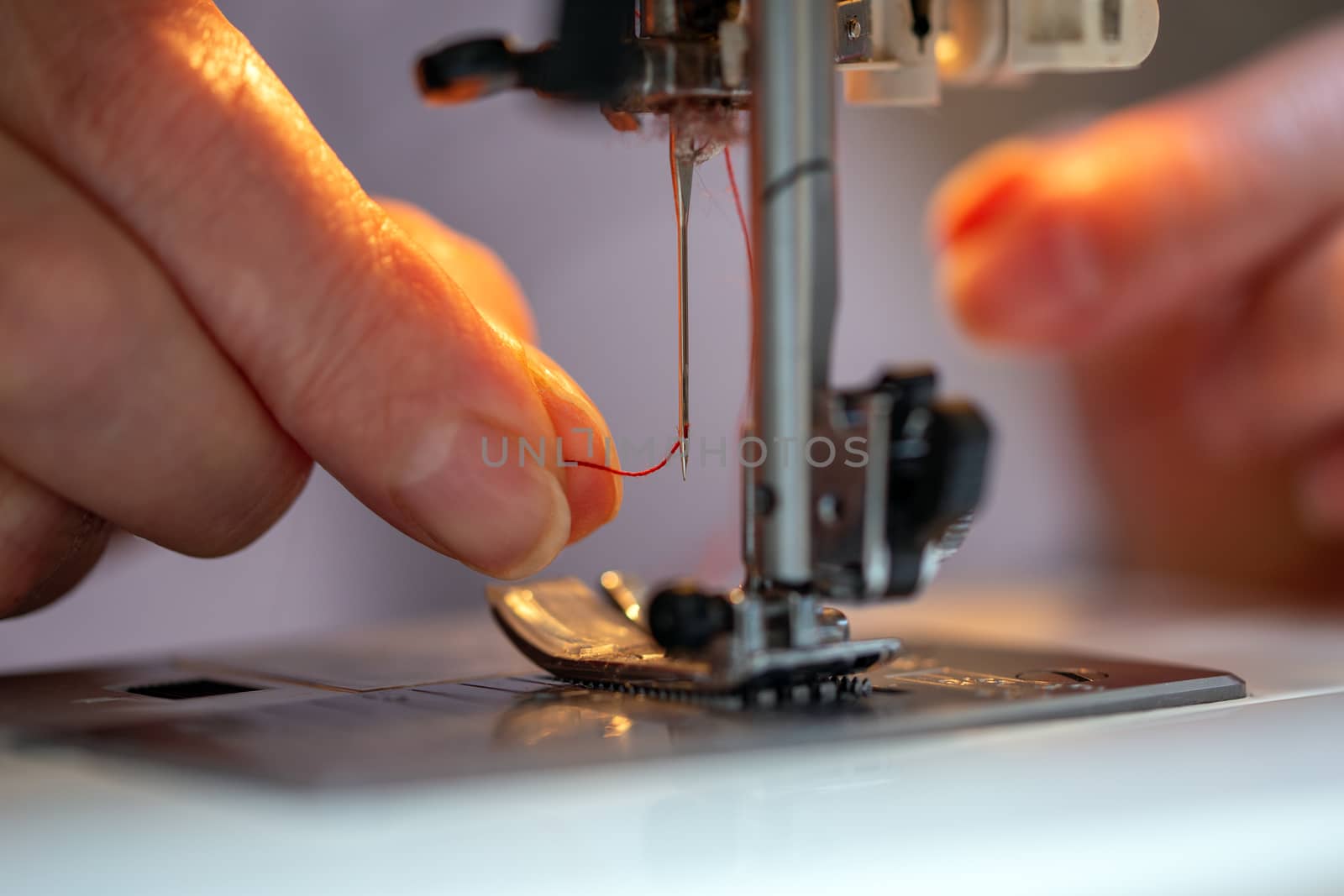 grandma fingers inserting a red thread into a sewing machine needle, close-up with selective focus