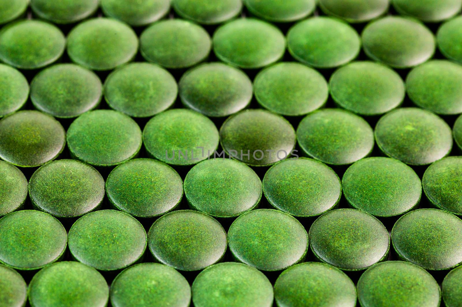 close-up background of many green organic spirulina tablets laid tight in one layer on flat surface.