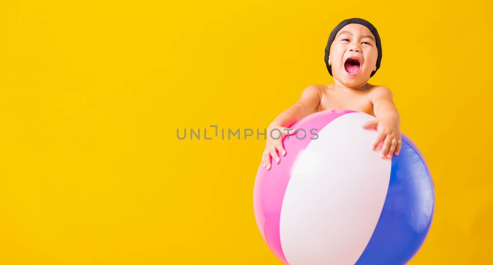 Summer vacation concept, Portrait Asian happy cute little child boy smiling in swimsuit hold beach ball, Kid having fun with inflatable ball in summer vacation, studio shot isolated yellow background