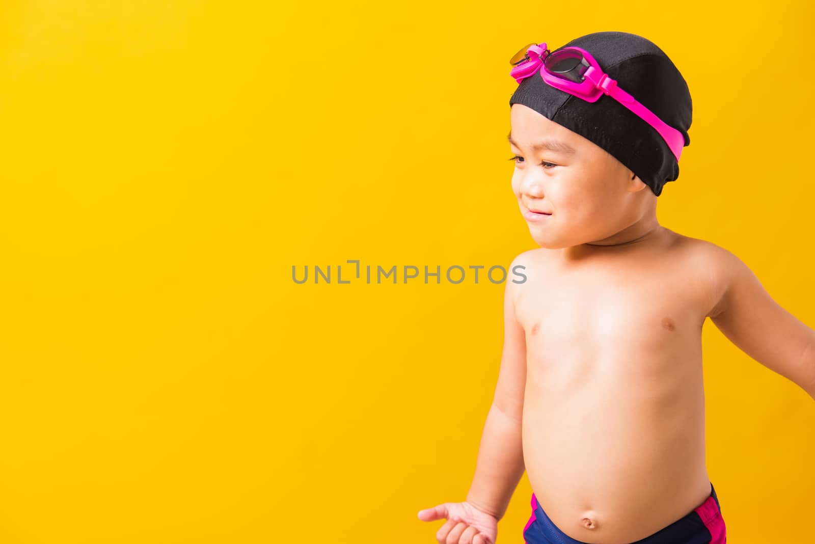 Summer vacation concept, Closeup portrait Asian happy cute little child boy wearing goggles and swimsuit, Kid having fun with in summer vacation looking side, studio shot isolated yellow background