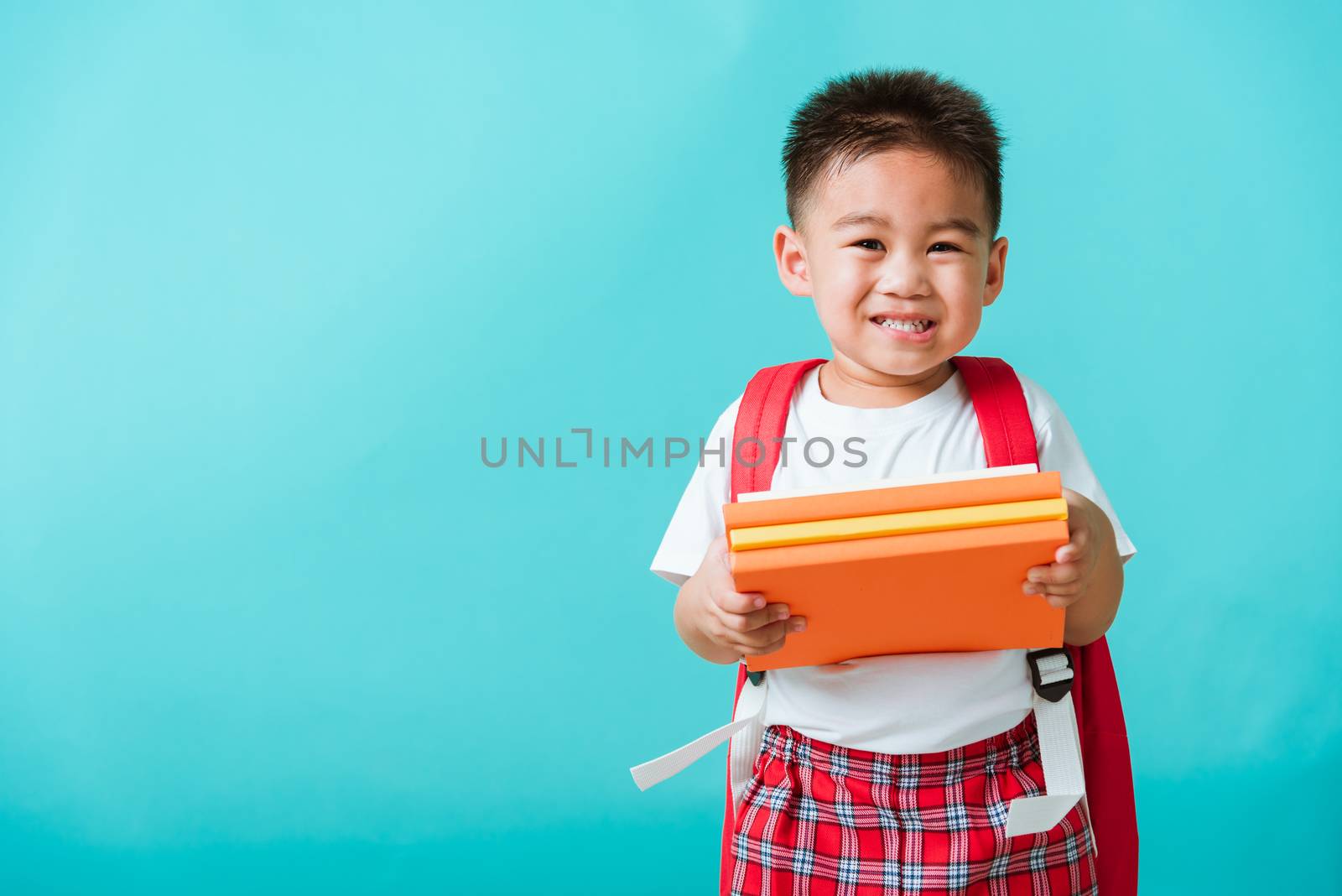 Back to school. Portrait Asian happy funny cute little child boy smiling and laugh holding books, studio shot isolated blue background. Kid from preschool kindergarten with school bag education