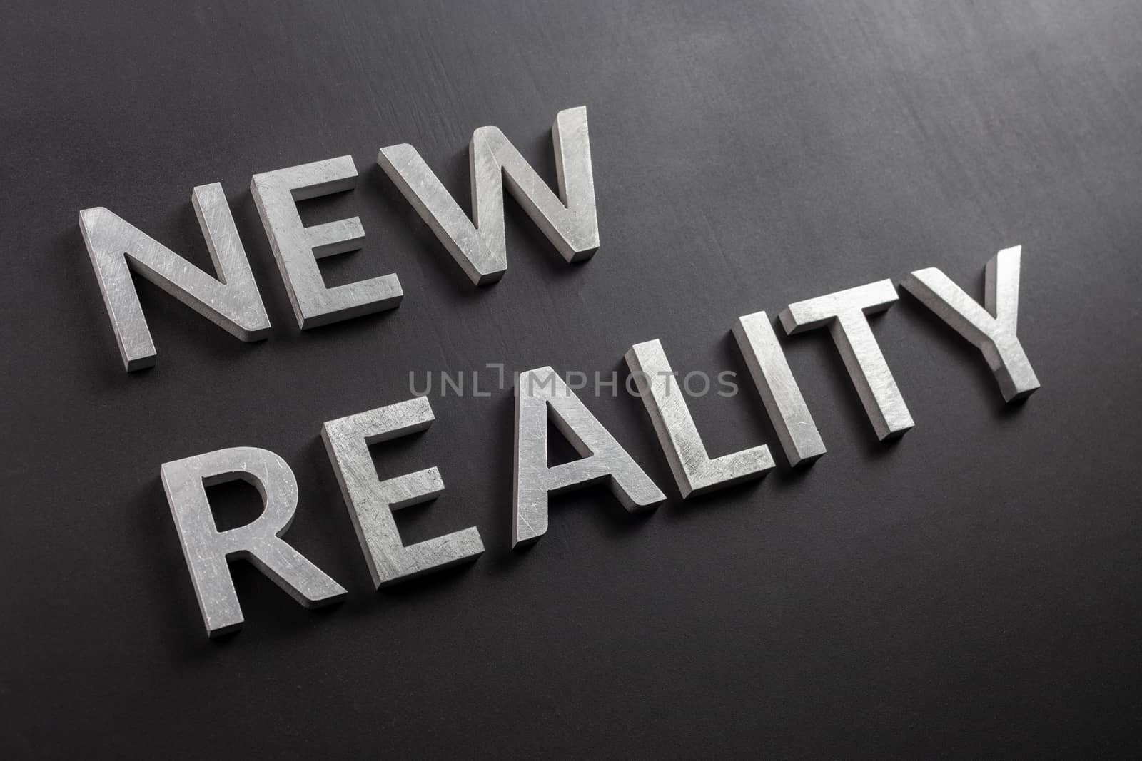 the words new reality laid with silver metal letters on flat black matte surface in slanted diagonal perspective.