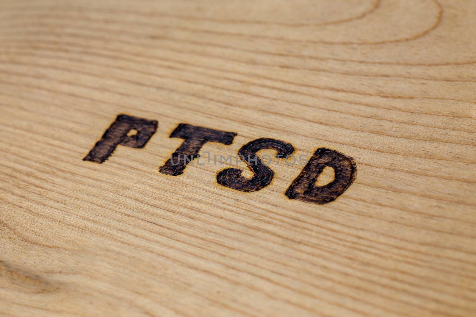 An abbreviation PTSD - post traumatic stress disorder - burned by hand on flat wooden board in diagonal composition. Close-up with selective focus.