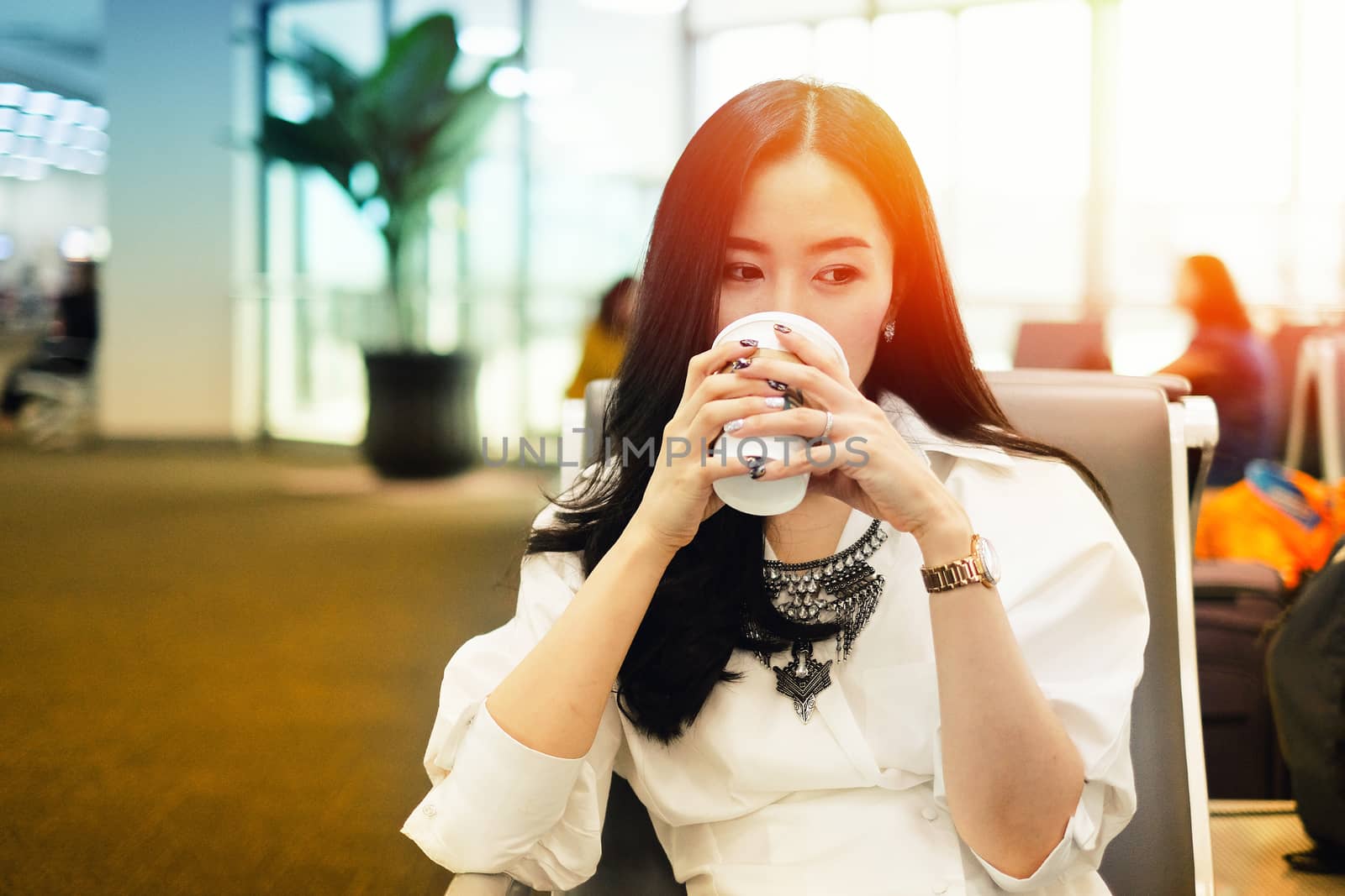 Woman drinking coffee while waiting to board at the airport by Surasak