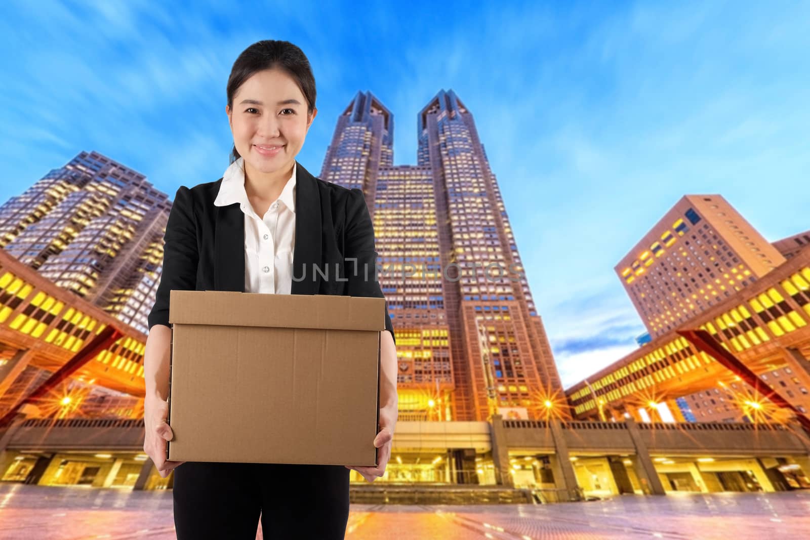 A young woman carrying a box wtih smile in night cityscape background

