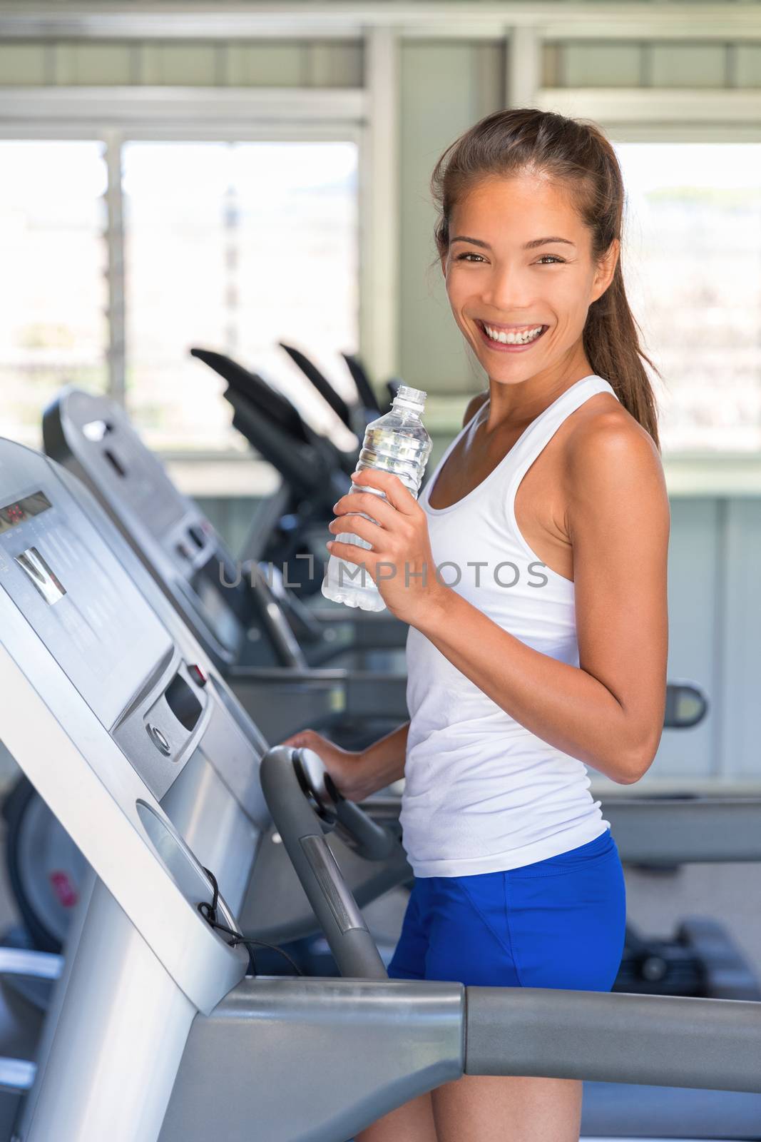 Runner woman drinking water in gym. Asian girl on running treadmill by Maridav