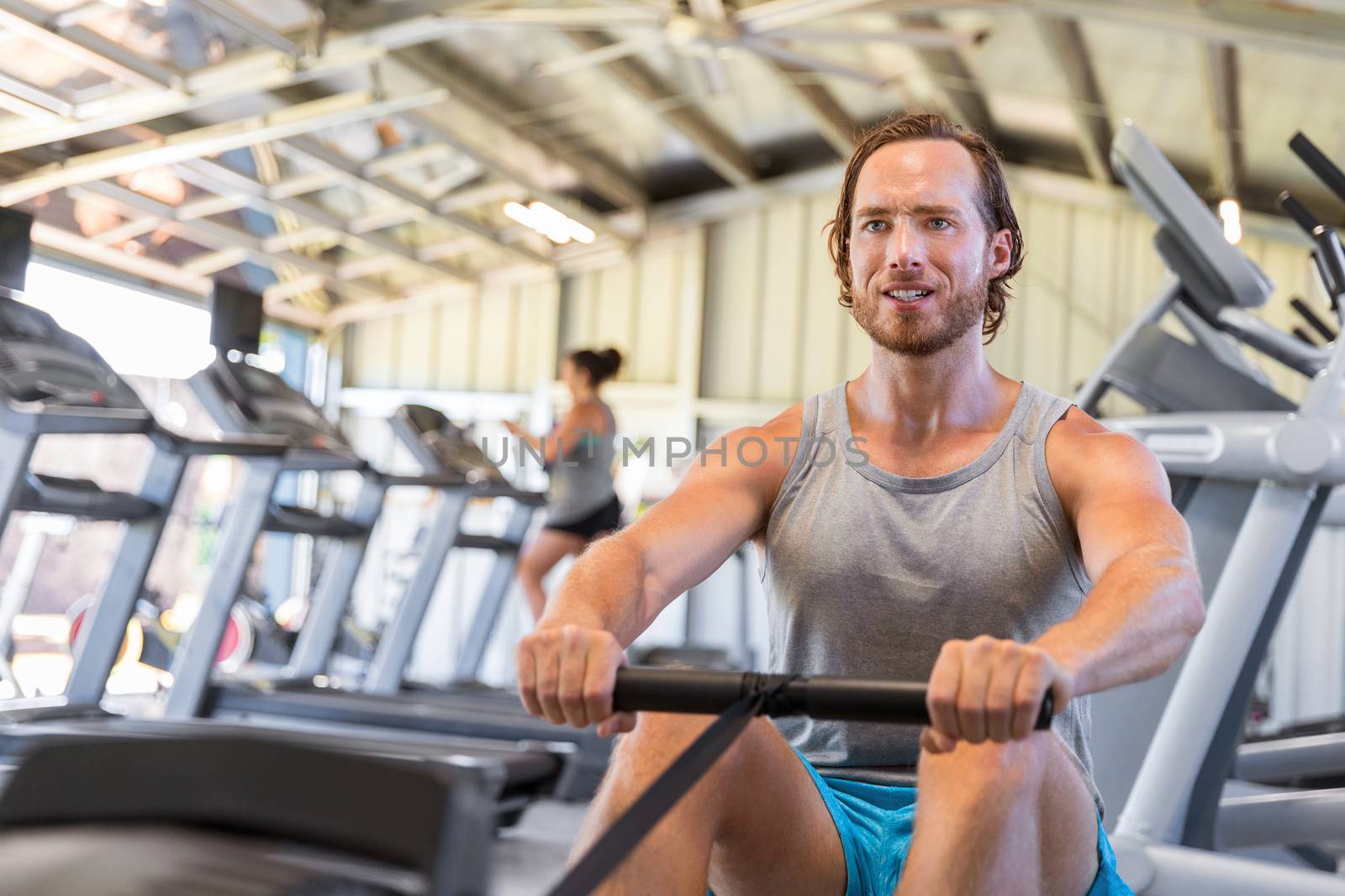 Man athlete training cardio on rowing machine in fitness gym.