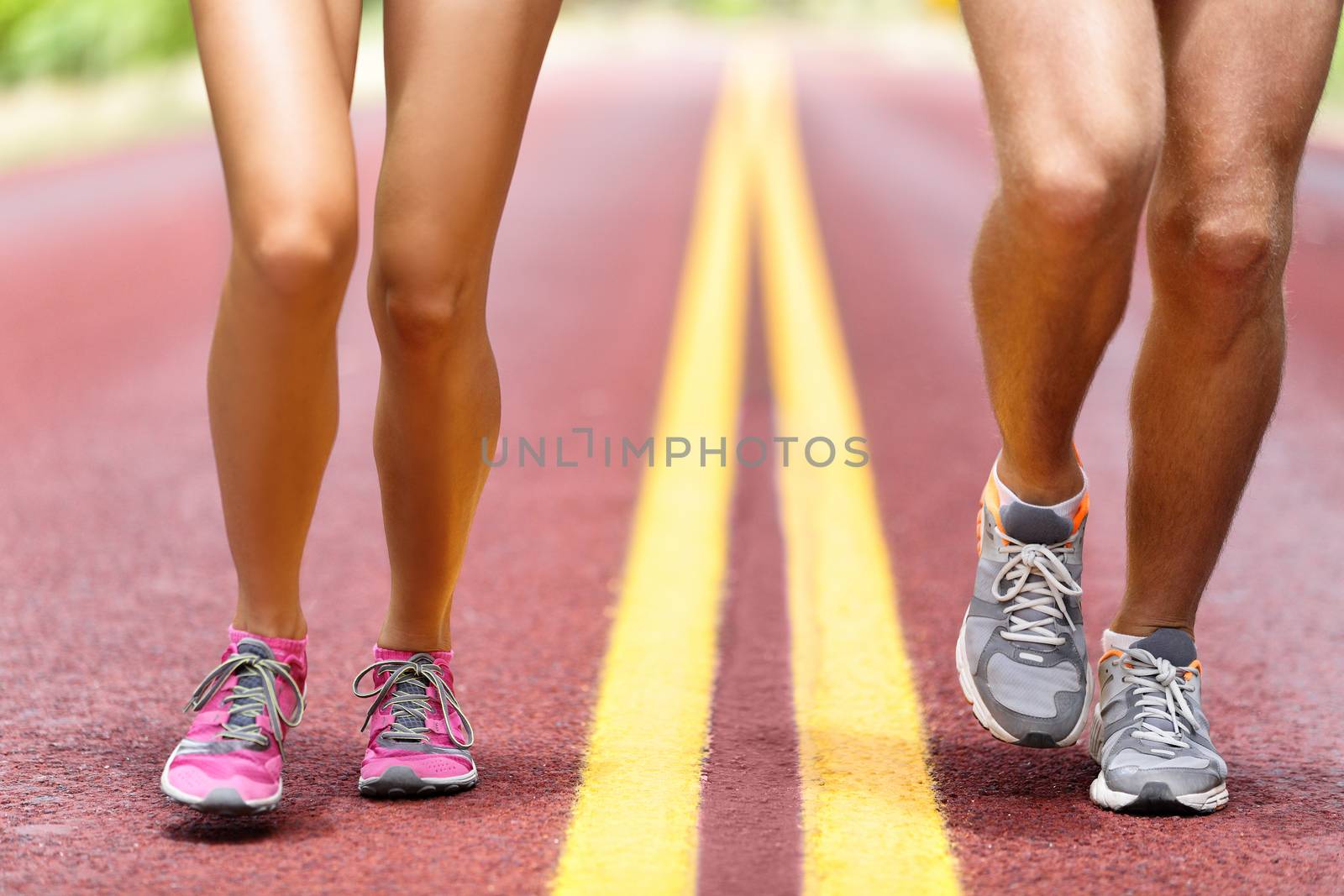 Man and woman running on road. Low section of sporty male and female are wearing sports shoes. Athletic runners are exercising on sunny day.